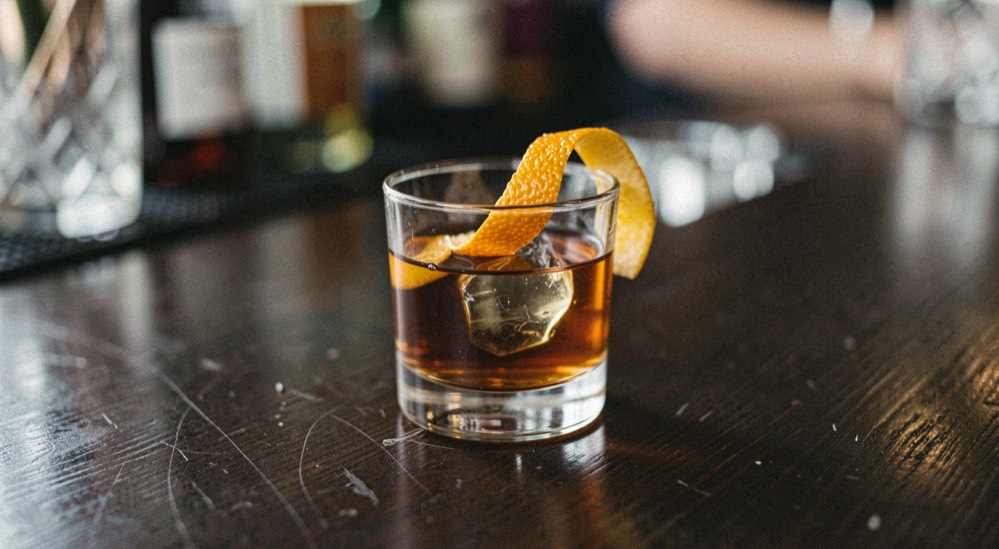 A short whiskey cocktail with orange peel on a dark bar top